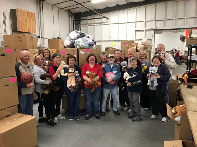A group of people posing with stuffed animals in a warehouse.