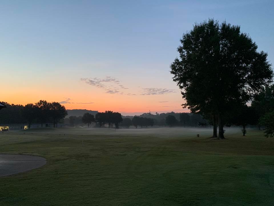 A golf course with trees and mist at sunrise.