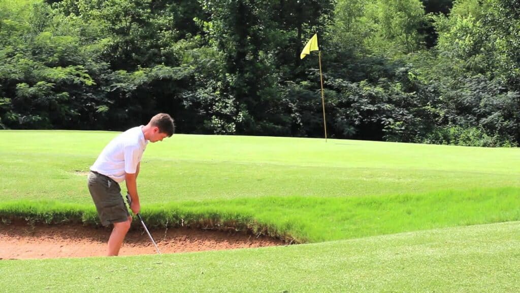 A young man hitting a golf ball out of a sand bunker.