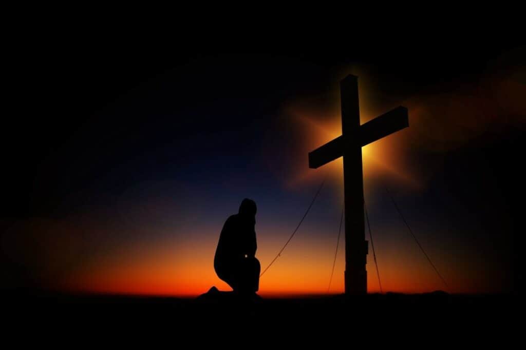 A silhouette of a person kneeling at the cross.
