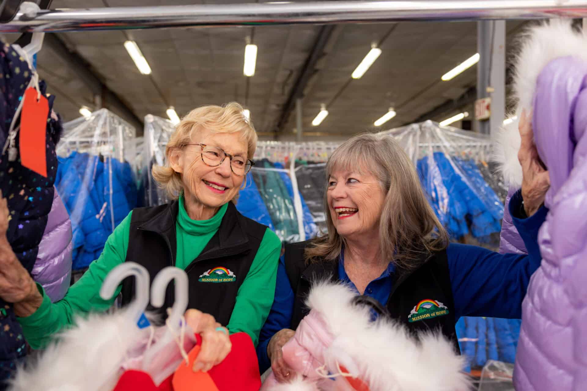 Two women looking at jackets in a warehouse.