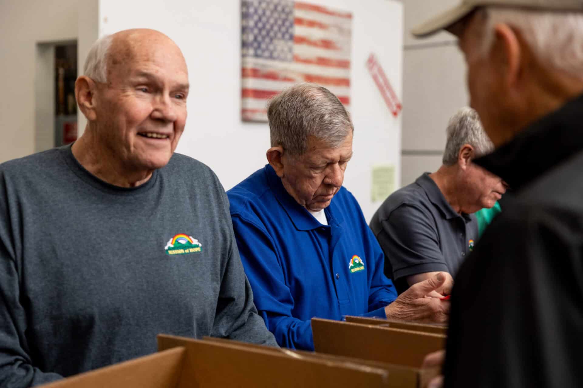 A group of older men standing in a warehouse being volunteers and happy.