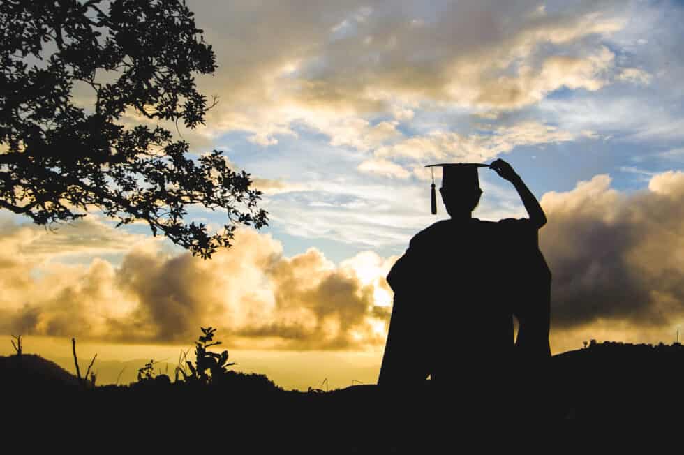 A silhouette of a person holding a graduation cap at sunset.