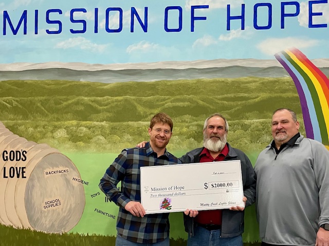 Three men standing in front of a mural with the words mission of hope.
