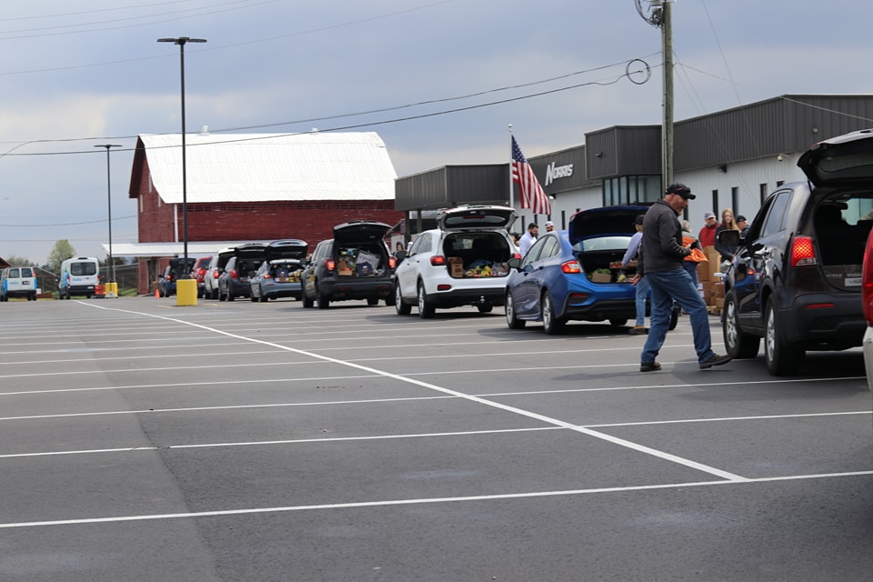 A parking lot scene showing vehicles lined up and a person walking across with flags in the background.