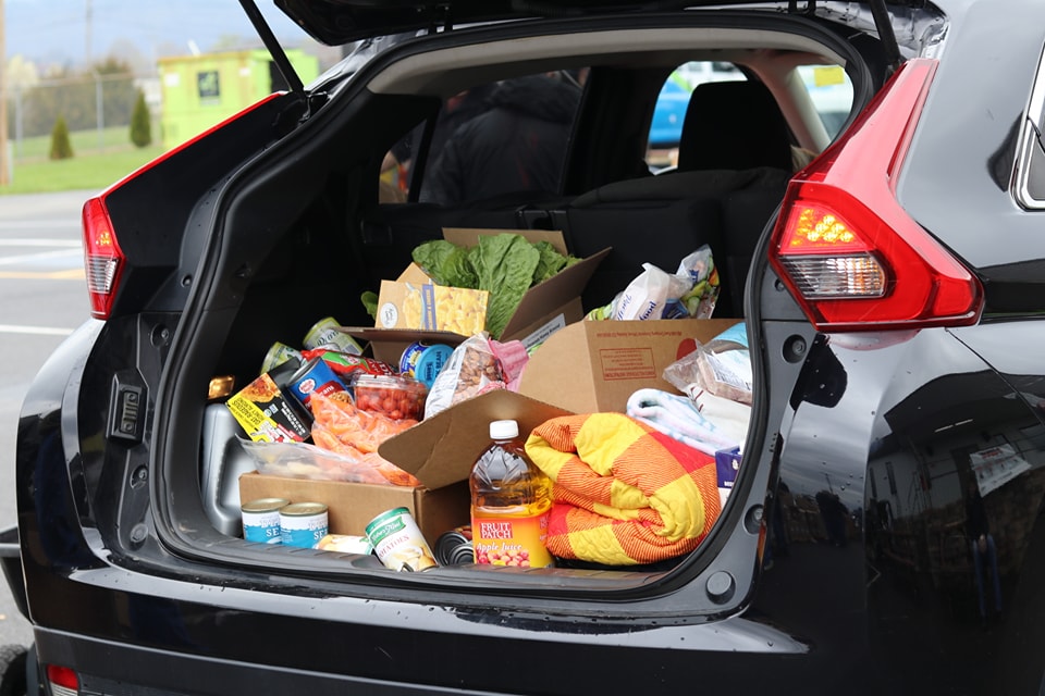 Open trunk of a car filled with various groceries including fresh produce, canned goods, and a large bottle of juice.